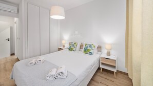 Et moderne hotelværelse med en pænt redt seng, et natbord med lampe og et garderobeskab.