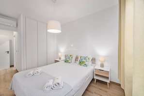 Ein modernes Hotelzimmer mit einem ordentlich bezogenen Bett, einem Nachttisch mit Lampe und einem Kleiderschrank.