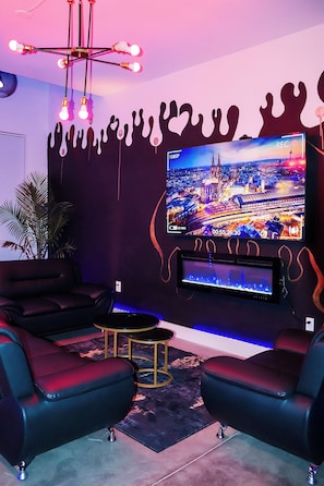 Un salon moderne doté d’un grand téléviseur à écran plat, de canapés en cuir noir, d’une petite table ronde et d’un décor mural original.