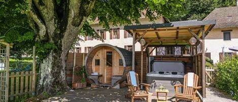 Een houten terras met buitenmeubilair, een jacuzzi en een houten constructie met een deur.