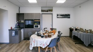 Un comedor con una mesa preparada para cuatro, una zona de cocina con electrodomésticos y una pared decorada con un cuadro.