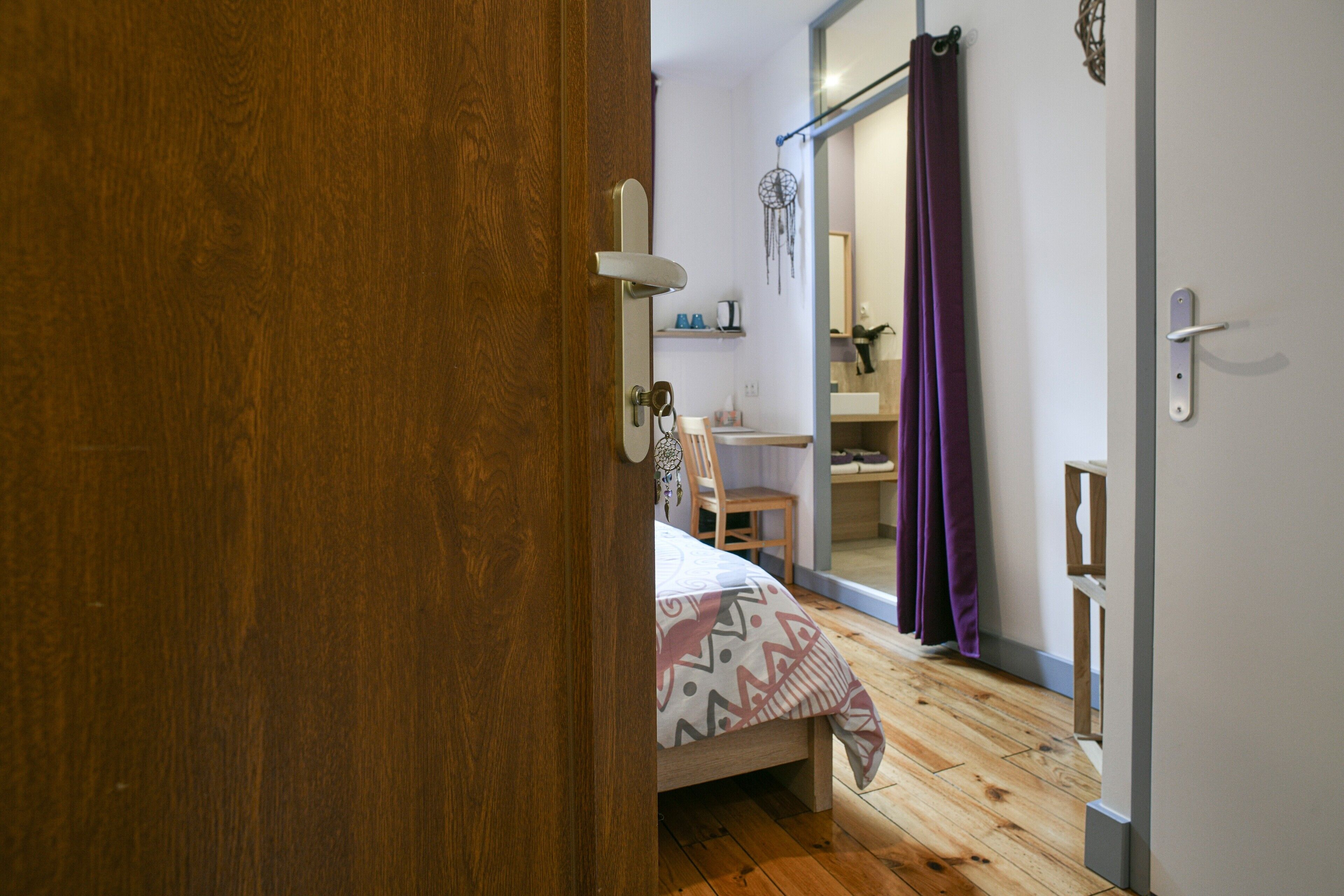 Ein Schlafzimmer mit Holzboden, einem Bett mit gemusterten Textilien, einem Sessel, einem Schreibtisch und einem Spiegel.