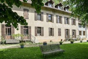 A building labeled 'SAINTE ANNE' with a garden, a bench, and potted plants.