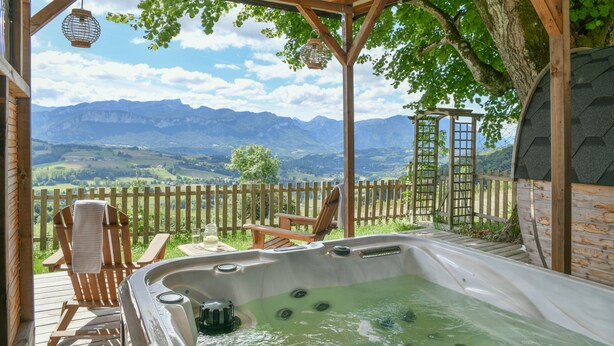 Een hottub met een houten terras, stoelen en uitzicht op bergen.