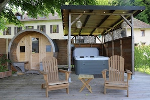 Une terrasse en bois avec deux fauteuils Adirondack, un jacuzzi et un espace couvert agrémenté de tissu à rayures zébrées.