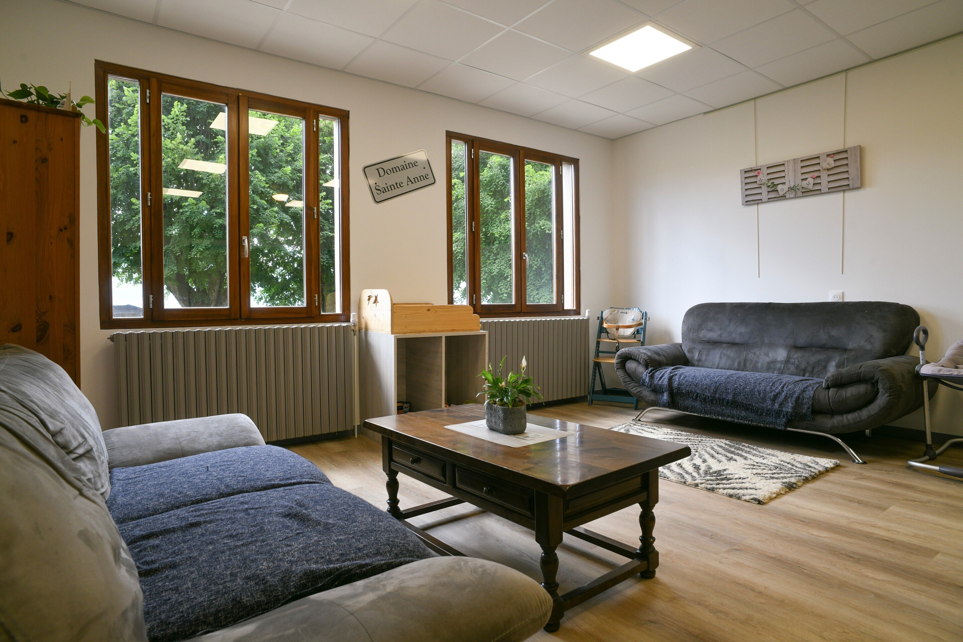 Una sala de estar con un sofá, una mesa de centro, una silla y ventanas amplias que dan a vistas de árboles.