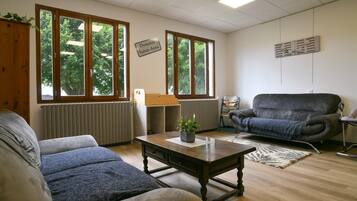 Una sala de estar con un sofá, una mesa de centro, una silla y ventanas amplias que dan a vistas de árboles.