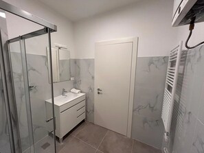 A bathroom with a glass shower enclosure, a white sink, and a door. - Apartment 'Appartamento Corte' with Wi-Fi and Air Conditioning (Gorizia)