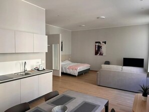 Una habitación moderna y minimalista con kitchenette, una cama, un sofá y un comedor.