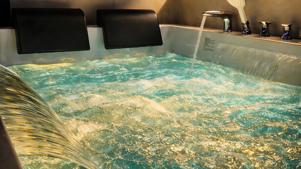 Jacuzzi con chorros de agua, cabezal de ducha y pared con azulejos.