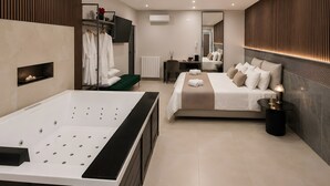 Habitación de hotel moderna con una bañera grande, una cama con muchas almohadas, un pequeño banco verde y una mesita de noche con lámpara.