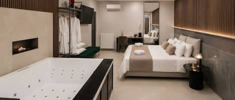 A modern hotel room with a large bathtub, a bed with multiple pillows, a small green bench, and a bedside table with a lamp.