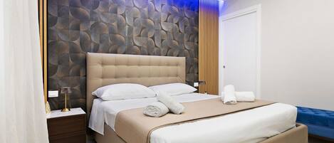 A modern bedroom with a large bed, a nightstand, a blue sofa, and a decorative wall.
