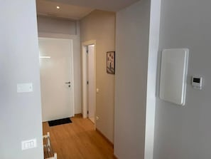 Un corridoio con pavimento in legno, pareti bianche, una porta e un termostato a parete.