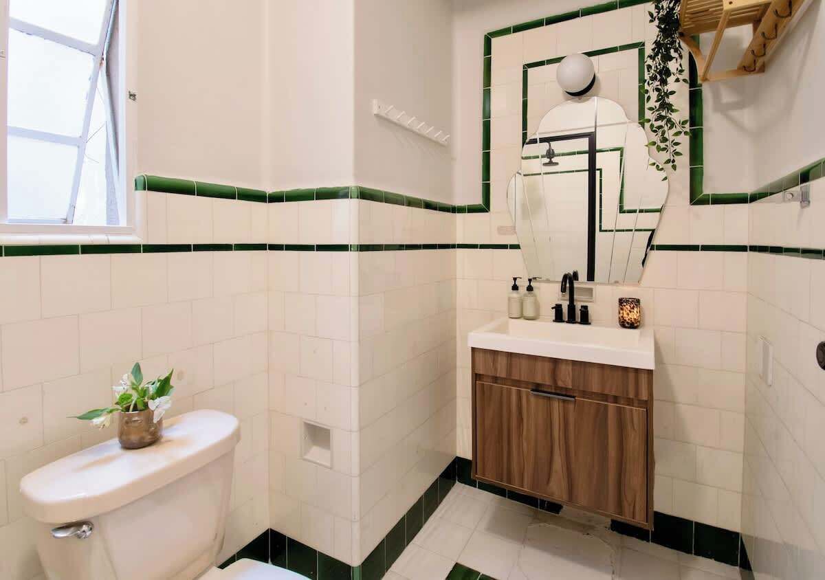 Ein Badezimmer mit Toilette, Waschbecken, Spiegel und grünen Fliesen.