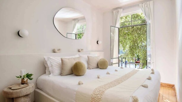 A bedroom with a bed, a round mirror, a window with a view of greenery, and a small table with a plant. - Breathtaking house with private rooftop in Condesa (Ciudad de México)