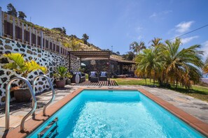 Une piscine bordée d’un muret en pierre, avec des chaises longues et une pergola.