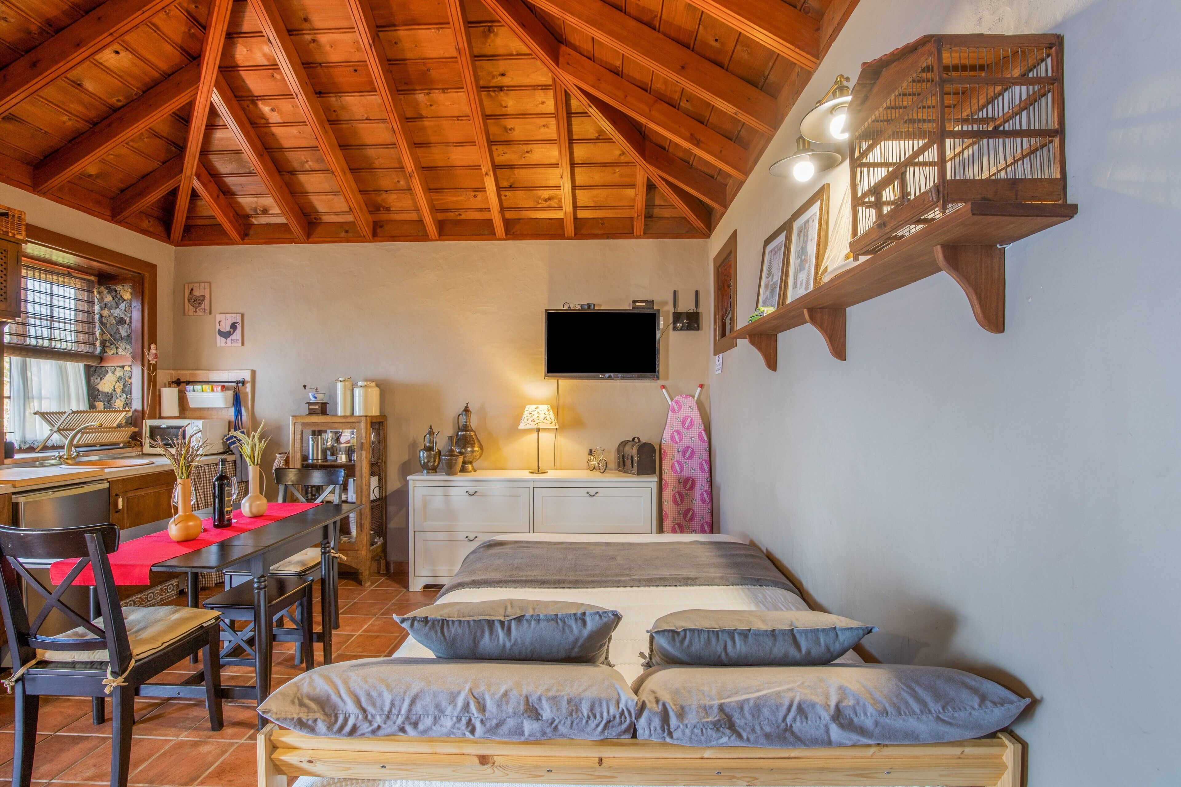 Une pièce avec un plafond en bois, un lit avec des oreillers, un bureau avec une chaise, une télévision et une étagère avec des objets décoratifs.