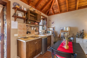 Une cuisine avec des meubles en bois, un évier, un réfrigérateur et une table à manger agrémentée d’un chemin de table rouge.