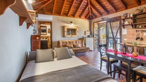 A bedroom with a large bed, a wooden ceiling, a dining area with a table and chairs, and a kitchen area with shelves and a counter. - Apartment 'Casa' with Sea View, Wi-Fi and Air Conditioning (Los Quemados)