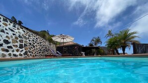 A swimming pool with clear blue water, a stone wall, and a palm tree. - Apartment 'Casa' with Sea View, Wi-Fi and Air Conditioning (Los Quemados)