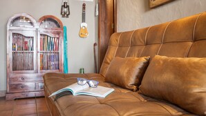 A brown leather sofa with a book and glasses on it, a wooden cabinet with books, and a guitar hanging on the wall. - Apartment 'Casa' with Sea View, Wi-Fi and Air Conditioning (Los Quemados)