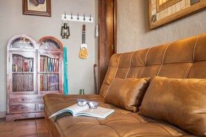 A brown leather sofa with a book and glasses on it, a wooden cabinet with books, and a guitar hanging on the wall.