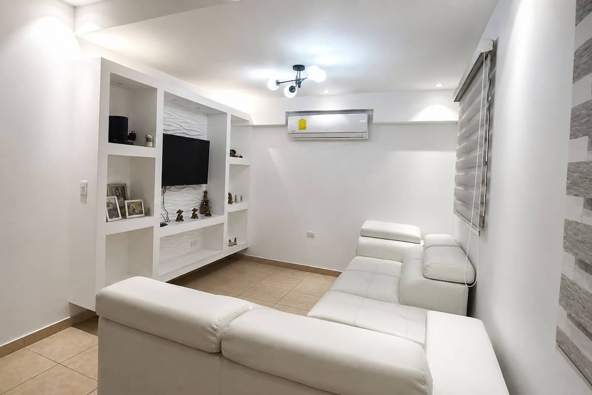 Un salon moderne avec un canapé blanc, un meuble de rangement intégré et un téléviseur à écran plat.
