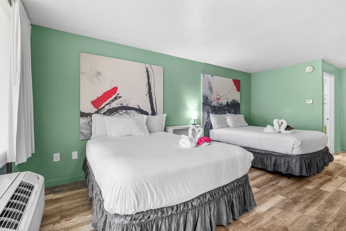 A hotel room with two beds, green walls, abstract art, and a wooden floor.