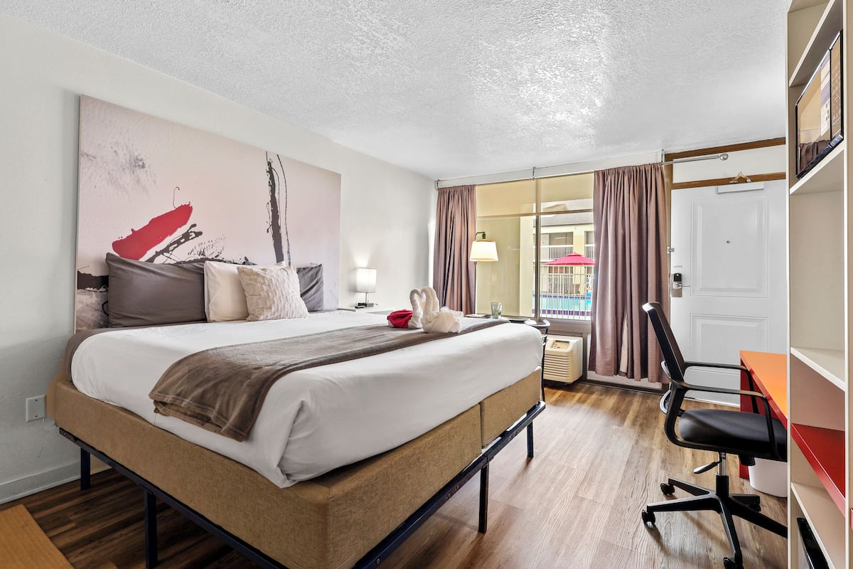 A hotel room with a bed, a desk, a chair, a lamp, and a window with curtains.