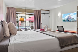 Una habitación de hotel con cama, escritorio, silla, televisor y ventana con cortinas.