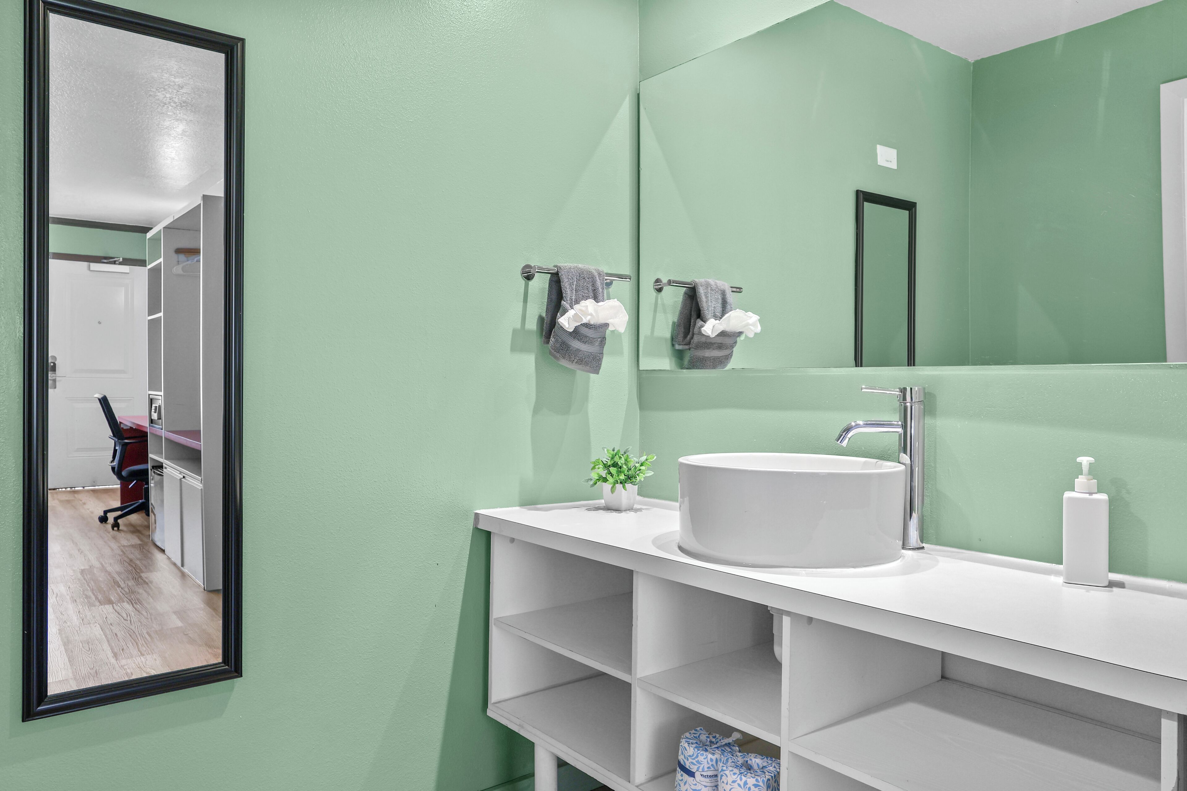 Un baño con un lavamanos blanco, un espejo y una pared verde.