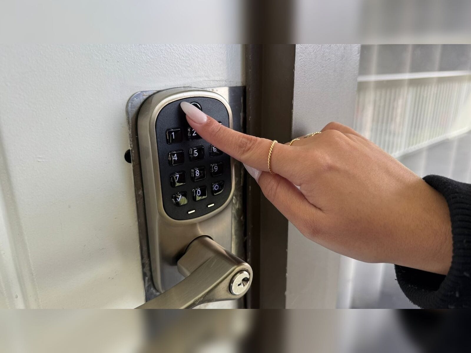 A hand pressing a numeric keypad on a door lock.