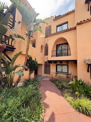 Une cour avec un chemin, un bâtiment doté de balcons et des plantes tropicales.