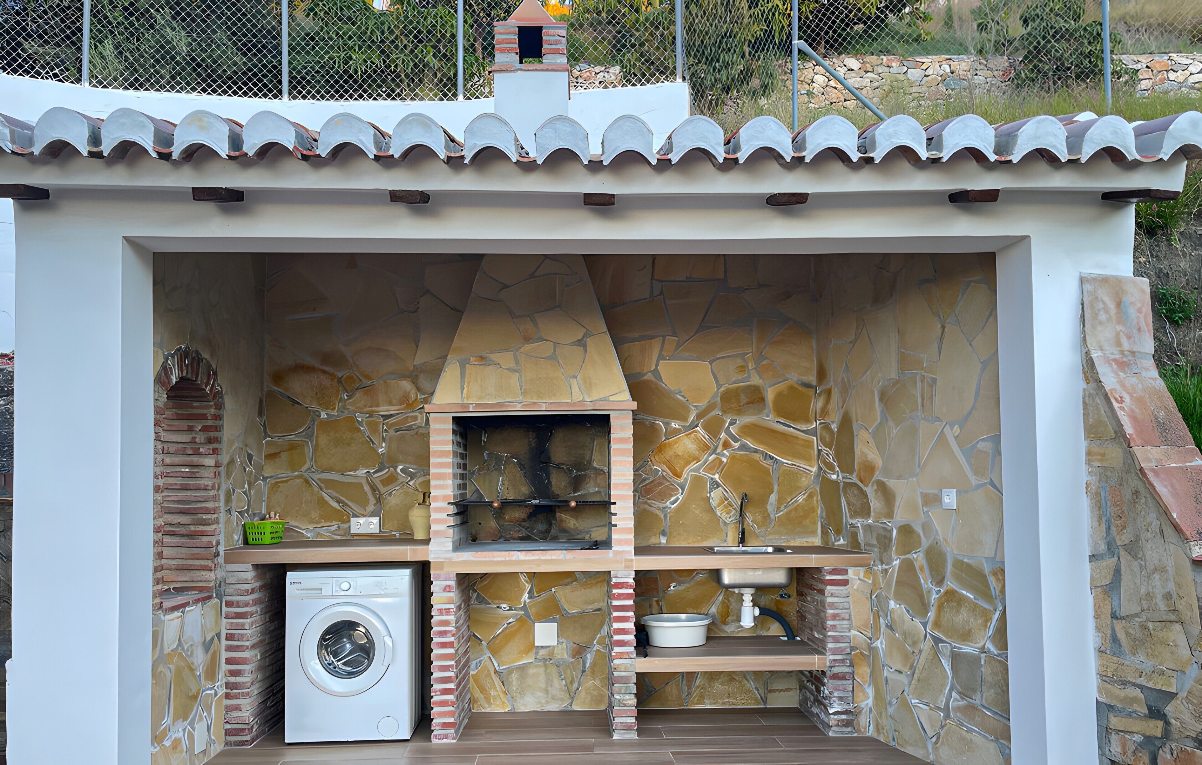 A compact outdoor kitchen with a stone wall, a washing machine, and a brick oven.