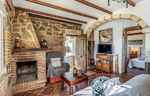 A cozy living room with a stone fireplace, wooden beams, a comfortable sofa, and a television. - Country House 'Villa El Tejo' with Sea Views, Wi-Fi, and Air Conditioning (Frigiliana)