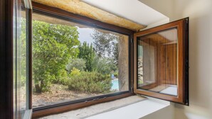 Une fenêtre donnant sur un paysage verdoyant, avec un bâtiment visible au loin.