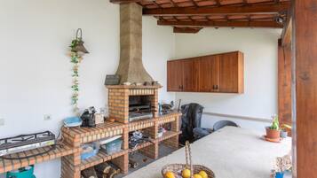 Uma cozinha ao ar livre construída com tijolos, com uma chaminé, uma mesa e um cesto de limões, além de um armário de madeira.