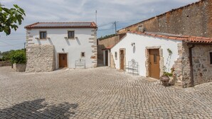 Un bâtiment traditionnel en pierre, doté d’une cour pavée, d’une porte en bois et d’un petit jardin.