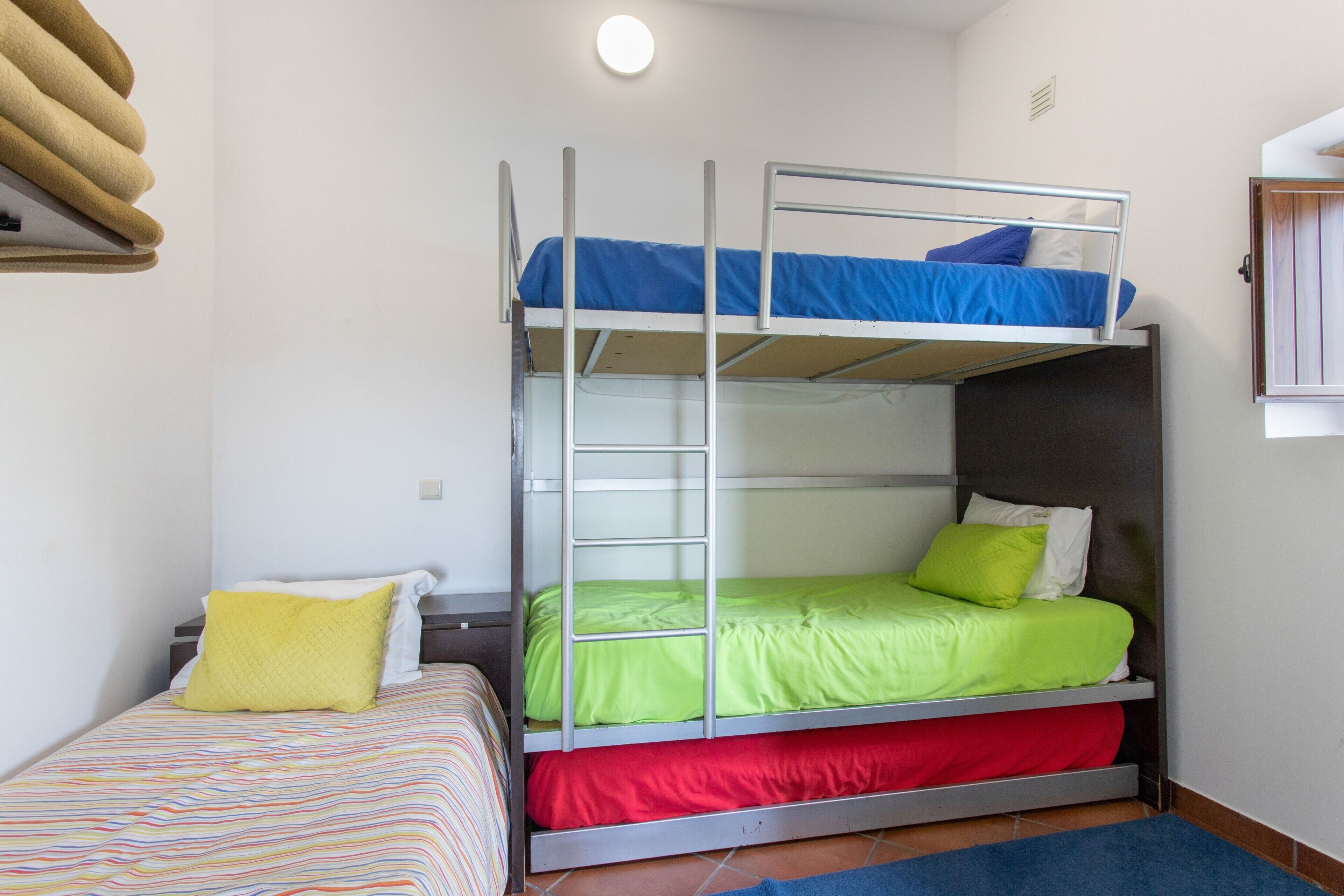 A bunk bed with a ladder, a single bed with a striped bedspread, and a blue rug on the floor.