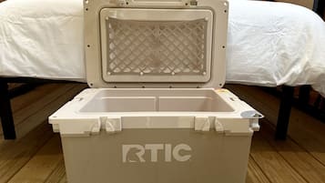 En vit, bärbar kylbox med varumärket ”RTIC” på sidan, placerad på ett trägolv.