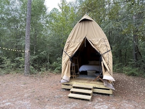 A tent with a ladder leading to a bed, surrounded by a forest.