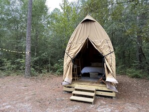 Una tenda con una scala che porta a un letto, immersa in una foresta.