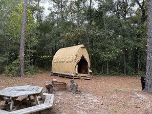 Une tente installée dans une forêt, avec une table de pique-nique et un foyer à proximité.