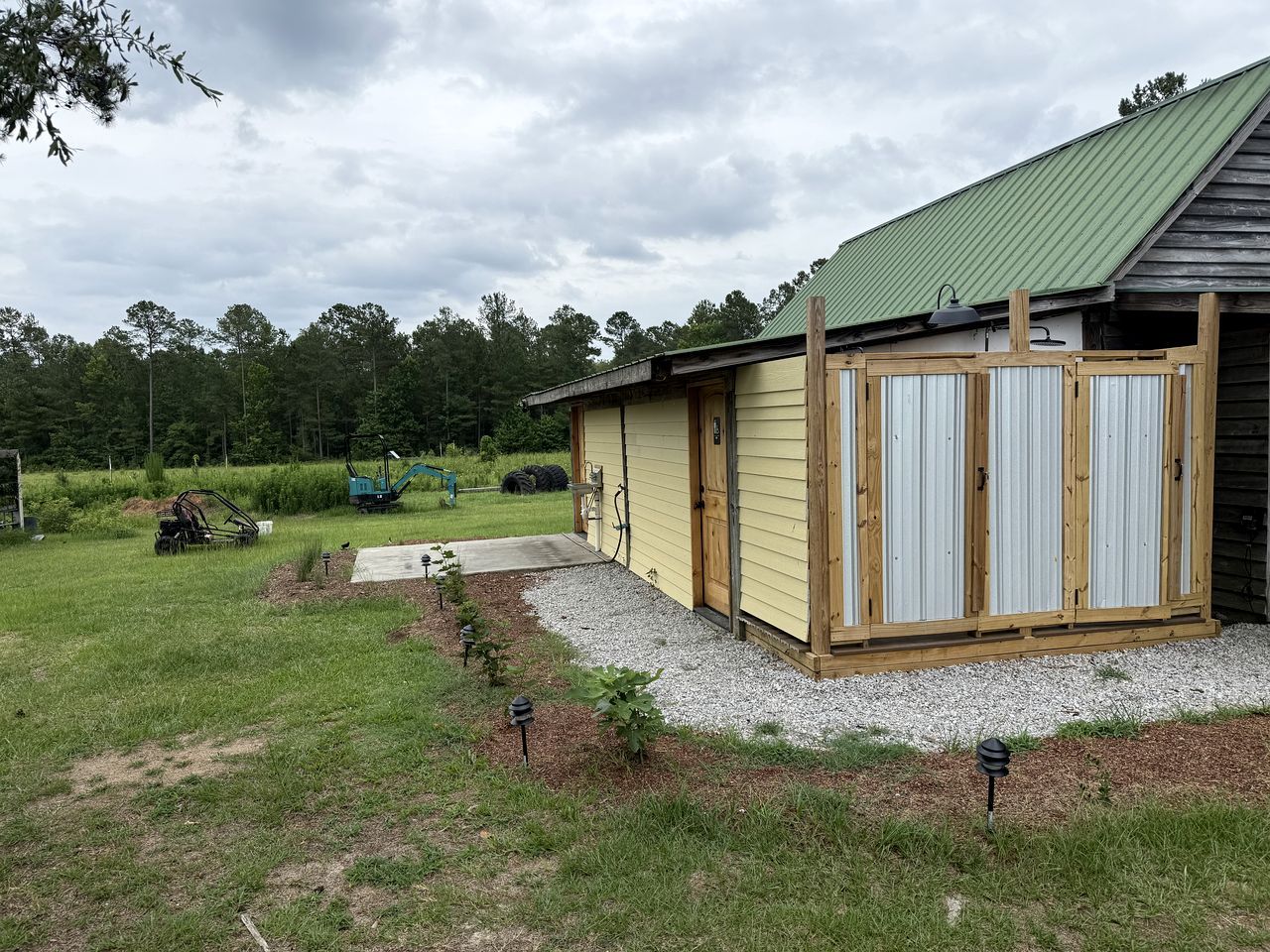 A single-story building with a green roof, a gravel driveway, and a small garden area with plants.
