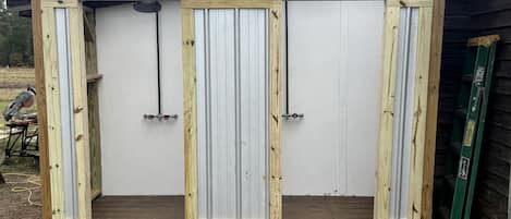 En träkonstruktion med tre vertikala paneler, troligen ett förvarings- eller utrymme för diverse ändamål, med en metalldörr och en stege som lutar mot den.