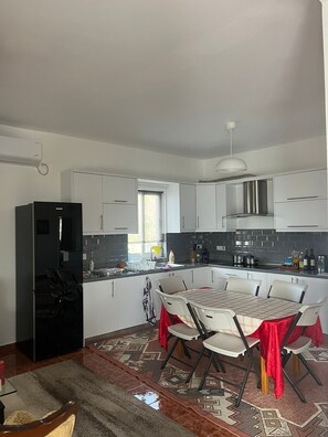 A modern kitchen with white cabinets, a black refrigerator, and a dining area with a table and chairs.