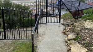 Camí cap a una entrada tancada amb vistes a una vila i muntanyes a la llunyança.