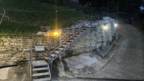 Una escala de pedra amb baranes metàl·liques que s'enfila cap a una collada, envoltada de vegetació.
