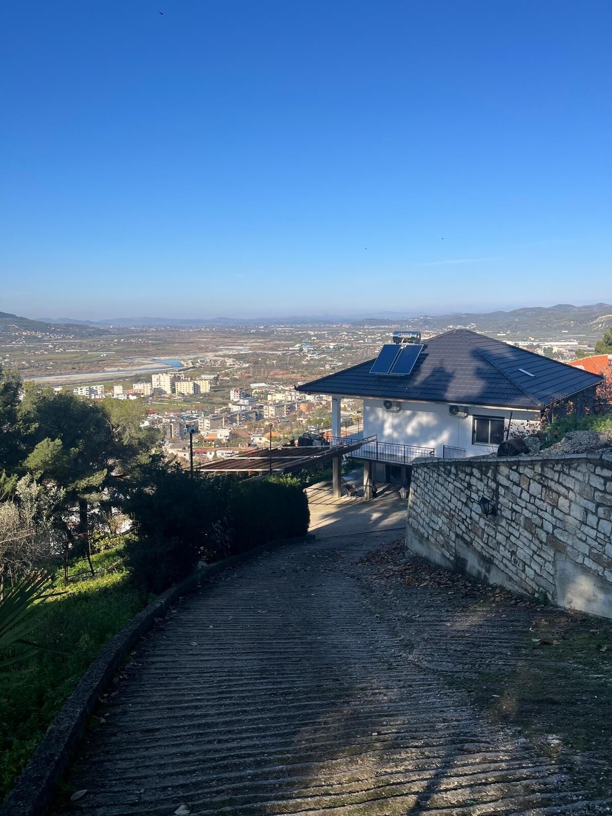 A building with a sloped roof, a stone wall, and a paved pathway leading to it.